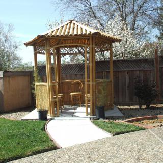 A wooden gazebo with a pathway in a landscaped garden setting.