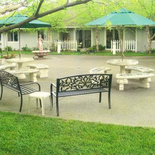 A peaceful outdoor courtyard featuring benches and tables with umbrellas, surrounded by greenery.