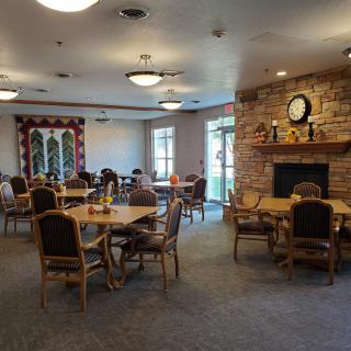 An empty dining room with tables and chairs, featuring a fireplace and decorative elements.