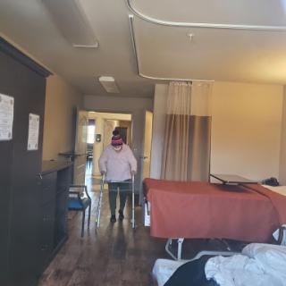 A view of a hospital room with a patient walking in the corridor.