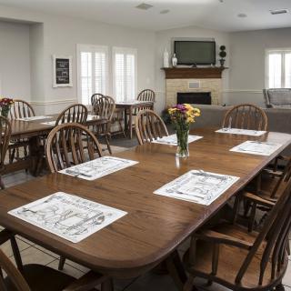 A clean and well-organized dining room with wooden tables and chairs, set with placemats and decorated with a vase of flowers.