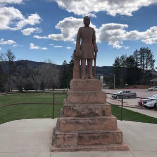 A statue standing against a backdrop of clouds and mountains, symbolizing history and remembrance.