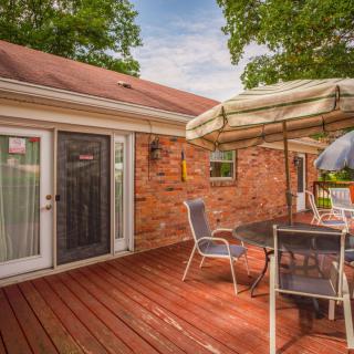 A cozy outdoor deck with a dining set under an umbrella, adjacent to a brick house.