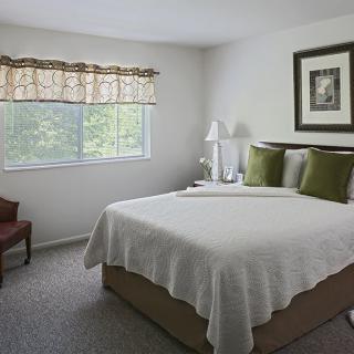 A cozy bedroom with a neatly made bed, a window letting in natural light, and simple decor.