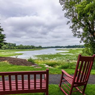A peaceful lakeside view with red chairs and a bench under a cloudy sky.