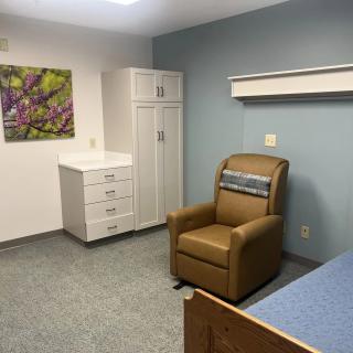 A hospital room with a bed, chair, and storage cabinet.