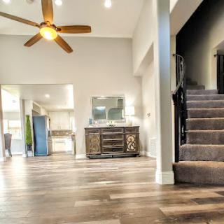 A bright and spacious living room featuring a ceiling fan, wooden flooring, and a staircase leading to the upper level.