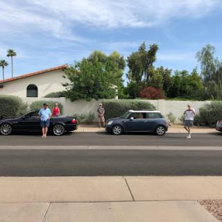 A group of people interacting near parked cars on a sunny day.