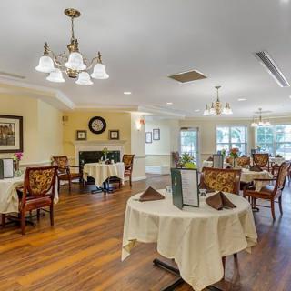 An elegantly decorated dining room with several tables and chairs, featuring a chandelier and large windows.