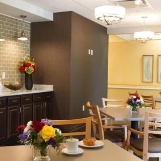 A cozy dining area with tables and chairs, adorned with flower arrangements and warm lighting.