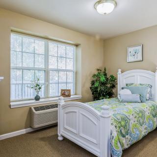 A cozy bedroom with a single bed, green bedding, and a large window letting in natural light.