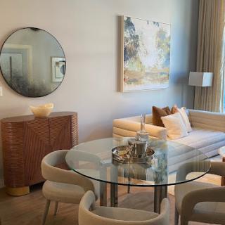 A stylish and modern living room featuring a glass dining table, comfortable seating, and elegant artwork.