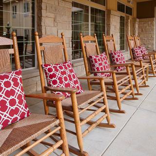 Wooden rocking chairs with red patterned pillows lined up on a porch.