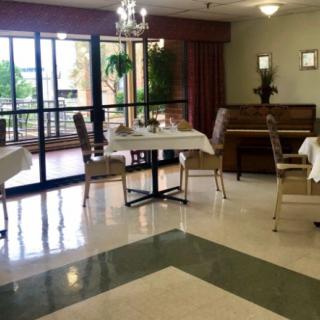 A quiet dining area with neatly arranged tables, chairs, and a piano by the window.