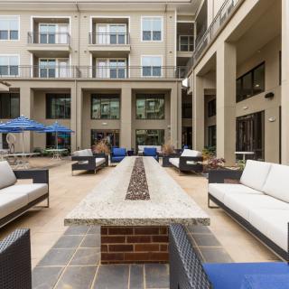 Modern outdoor seating area with couches and a central fire pit in an apartment courtyard.
