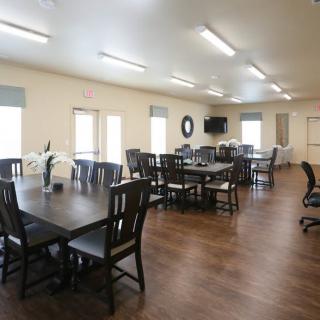 A spacious dining room with multiple tables and chairs, featuring wooden flooring and ample lighting.