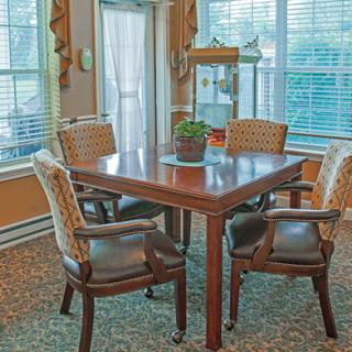A cozy dining area with a wooden table and four cushioned chairs, surrounded by large windows and adorned with a small potted plant.