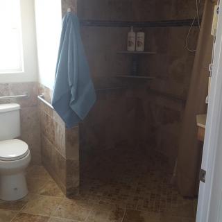 A bathroom with a tiled shower area, toilet, and a towel hanging near the window.