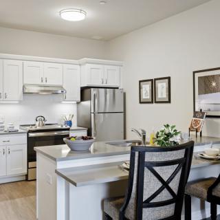 A modern kitchen with white cabinets and a dining area, featuring stainless steel appliances and elegant decor.