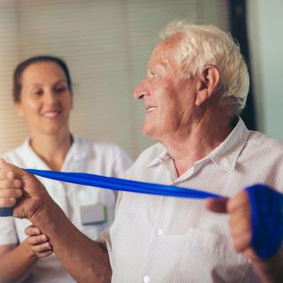 An elderly man engaging in physical therapy with the assistance of a healthcare professional.