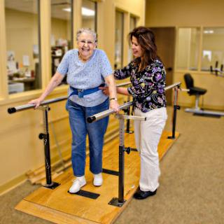 A physical therapist assisting an elderly woman during a walking exercise at a rehabilitation facility.