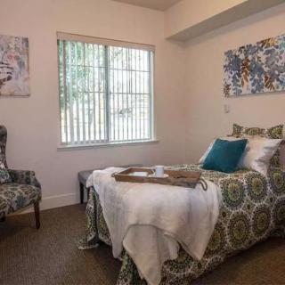 A cozy bedroom with a single bed, decorative pillows, a patterned chair, and artwork on the walls.