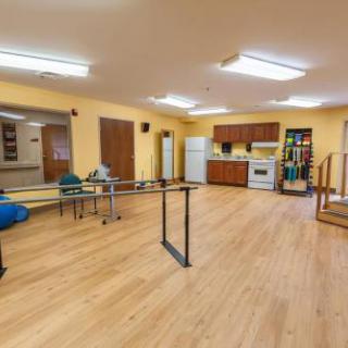 A spacious and well-lit rehabilitation room featuring a kitchenette and various furniture arrangements.
