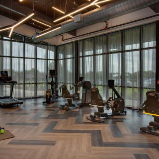 A modern gym with large windows, featuring treadmills and stationary bikes.