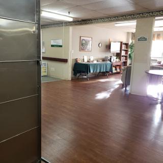 A spacious common area with wooden flooring and ample natural light, featuring seating and decor.