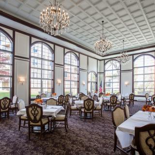 An elegant dining room with large windows, chandeliers, and neatly arranged tables and chairs.