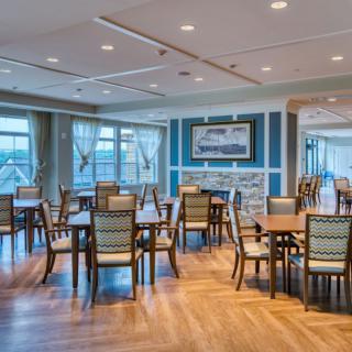A spacious dining area with neatly arranged tables and chairs, featuring wood flooring and ample natural light.