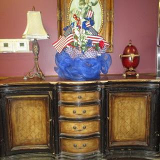A beautifully crafted wooden cabinet with decorative elements, including a lamp and a floral arrangement featuring small flags.