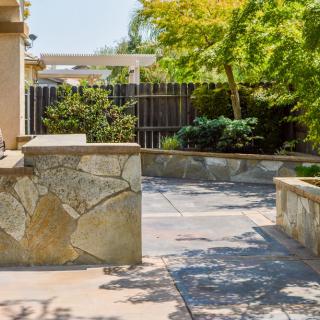A sunny patio area with stone walls and lush greenery in the background.