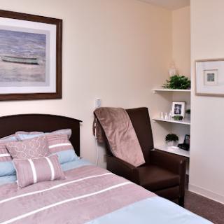 A cozy bedroom featuring a neatly made bed with striped bedding, a comfortable chair, and decorative wall art.
