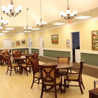 A spacious dining room with multiple tables and chairs, illuminated by elegant chandeliers.