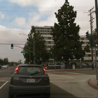 A view of an urban intersection with traffic and buildings under a cloudy sky.