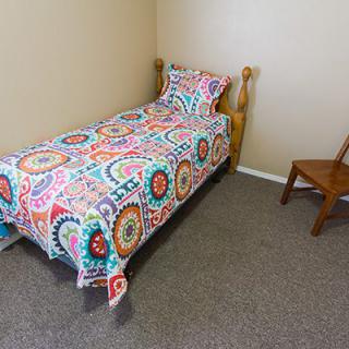 A simple bedroom with a colorful single bed and a wooden chair.