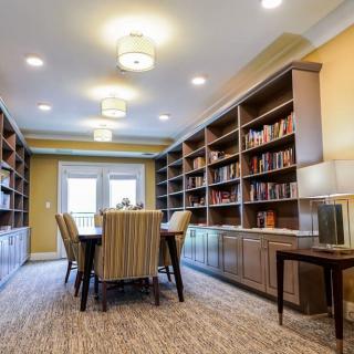 A cozy library room with bookshelves and a central table surrounded by chairs.