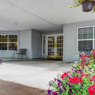 A welcoming building entrance with a porch adorned with vibrant flowers and a bench.