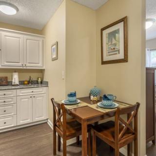 A cozy kitchen dining area with a small table set for two, complete with place settings and surrounded by white cabinets.