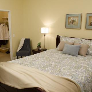 A cozy bedroom with a neatly made bed, decorative pillows, and soft lighting from a floor lamp beside the bed.