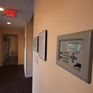 A hallway featuring a security control panel and an emergency exit sign.