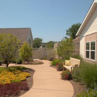 A beautifully landscaped garden with a winding pathway, surrounded by various shrubs, trees, and flowers. A bench is placed along the path for relaxation.
