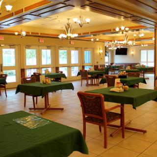 A spacious dining area featuring tables with green tablecloths and ample natural light from the windows.