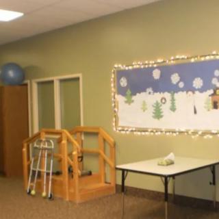 A rehabilitation room with physical therapy equipment, including walkers and crutches, next to a decorated bulletin board.