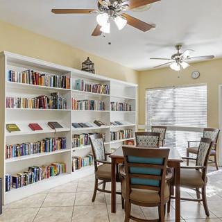 A cozy reading room with bookshelves, a table, and chairs under ceiling fans.