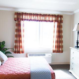 A cozy bedroom with a window, dressed bed, and decorative curtains.