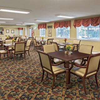 A spacious and elegant dining room with neatly arranged tables and chairs, featuring patterned carpet and decorative curtains.