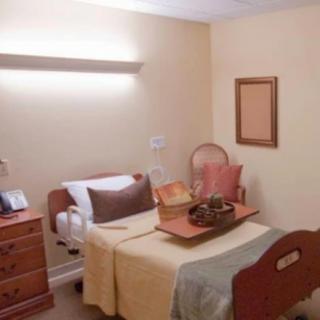 A simple bedroom with a hospital bed, bedside table, and minimal decor.