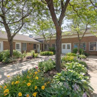 A peaceful courtyard garden with trees and flowers next to a brick building.